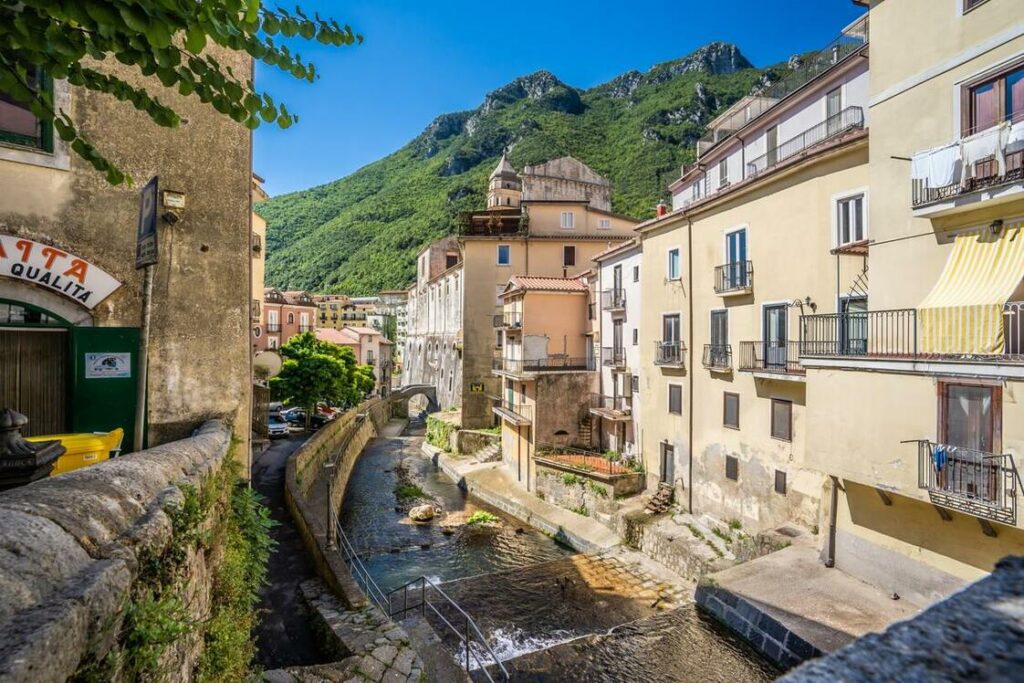 Sandy colored historic buildings either side of fast flowing river