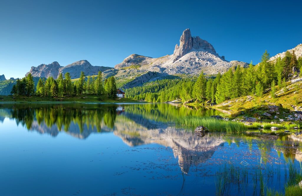 Mountains and trees beneath blue sky and mirrored in crystal clear lake