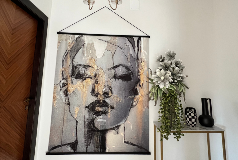 Large image on wall of ladies face next to plant on gold console table