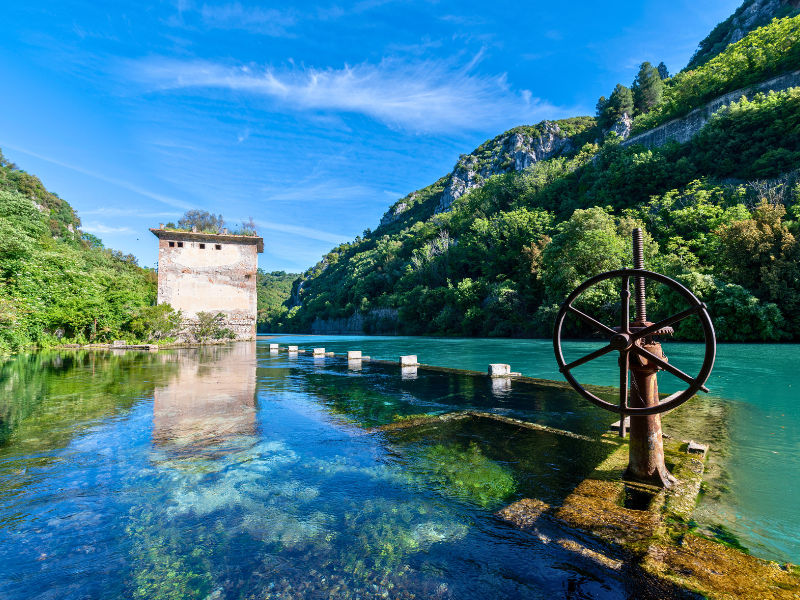 Clear blue and green water with a stone building and rusty wheel