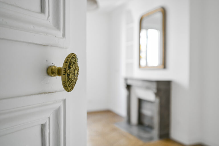 Door with gold handle opening to ornate fireplace and mirror