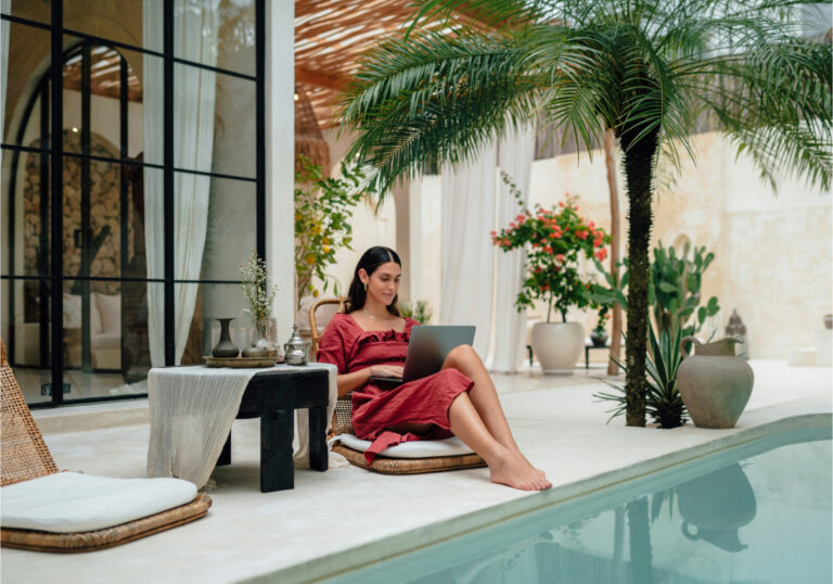 woman in red dress on laptop by luxury pool