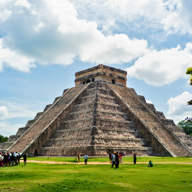 Chichen itza in Yucatan with tourists walking on green grass at the foot