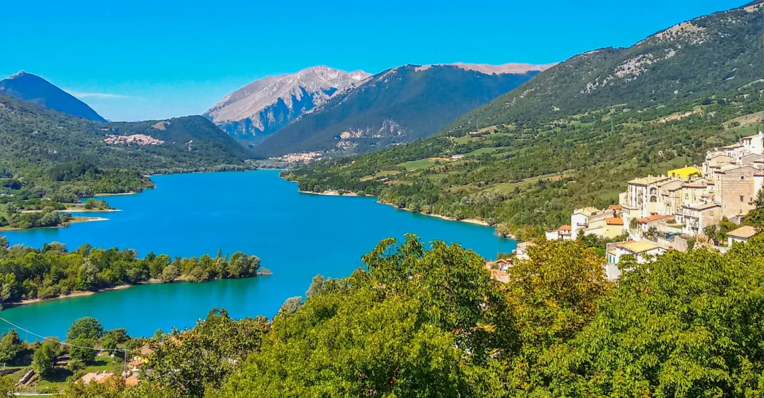 Abruzzo area guide: turquoise mountain lake at sunset with a hillside village of terracotta rooftops